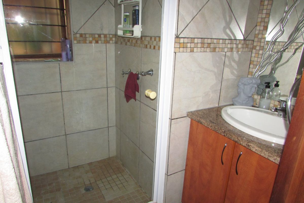A functional bathroom featuring a shower enclosure, vanity cabinet with granite countertop, and tiled finishes throughout.