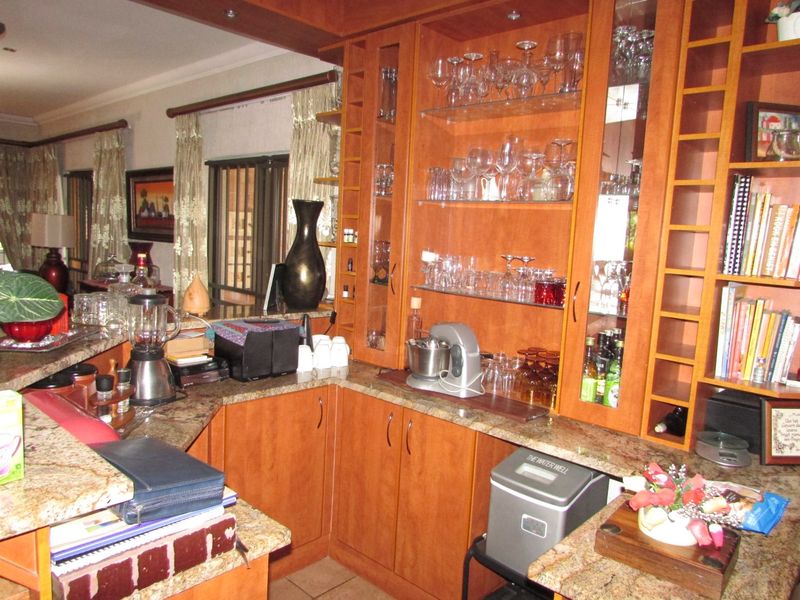 A kitchen area featuring warm-toned wooden cabinetry, granite countertops, and integrated glass display shelving for glassware storage.