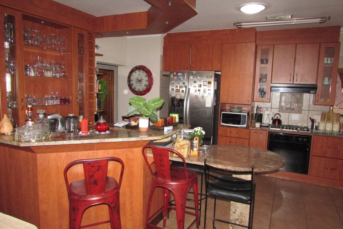 A functional kitchen featuring warm-toned wooden cabinetry, granite countertops, a breakfast bar, and integrated appliances including an oven and gas hob.