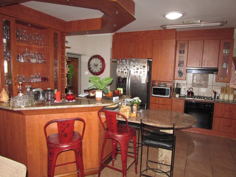 A functional kitchen featuring warm-toned wooden cabinetry, granite countertops, a breakfast bar, and integrated appliances including an oven and gas hob.