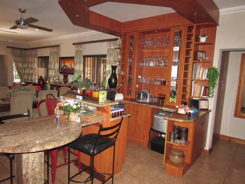 A dedicated home bar area featuring custom wood cabinetry, granite countertops, integrated glass shelving, and tiled flooring, seamlessly connected to the adjacent living space.