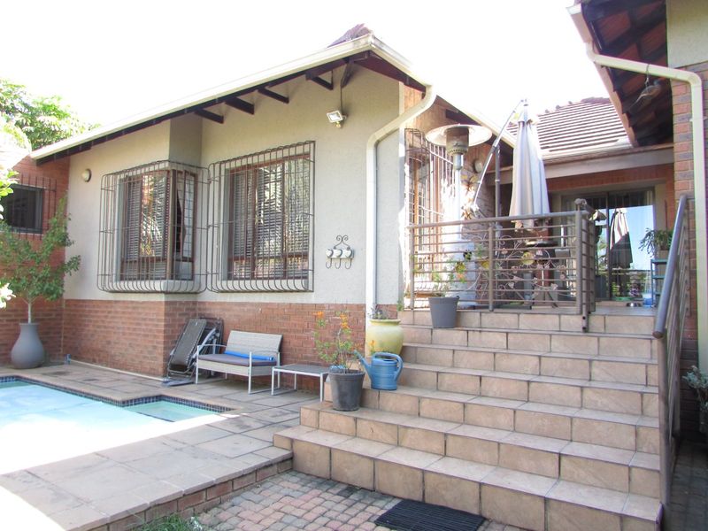 Rear exterior view featuring a swimming pool, tiled staircase, and brick-accented facade with security bars on the windows.