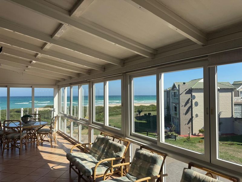 Enclosed patio featuring tiled flooring, exposed beam ceiling, and expansive sliding glass windows offering panoramic ocean and coastal views.