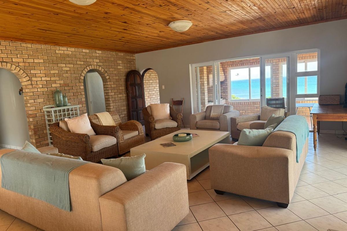 Spacious living room featuring exposed brick walls, a warm timber ceiling, tiled floors, and large sliding doors offering ocean views.
