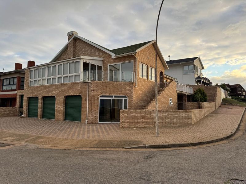 A multi-level face brick house featuring a triple garage, paved driveway, and an enclosed upper-level balcony with external staircase access.