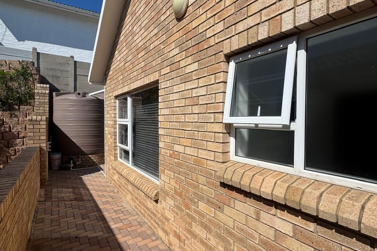 A side exterior view of the property featuring face brick walls, paved pathways, and a water storage tank.
