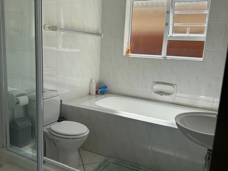 A functional bathroom featuring a built-in bathtub, separate glass shower enclosure, pedestal basin, and neutral ceramic tiling throughout.