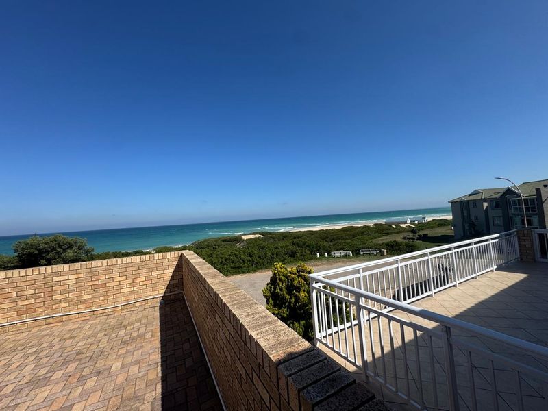 Spacious elevated balcony featuring brick parapet walls, tiled flooring, and white metal balustrades, offering expansive views of the coastline and ocean.