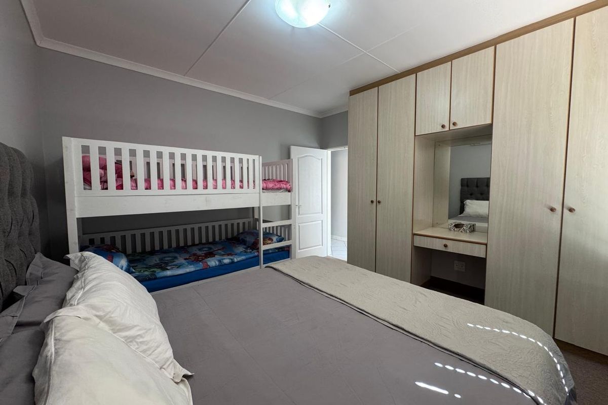 A well-maintained bedroom featuring extensive built-in cupboards with an integrated vanity area and neutral wall finishes.