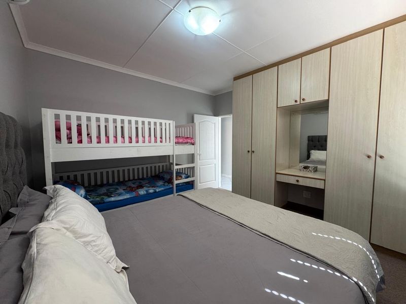 A well-maintained bedroom featuring extensive built-in cupboards with an integrated vanity area and neutral wall finishes.