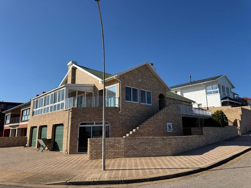 A multi-level brick house featuring a double garage, an elevated balcony with glass balustrades, and a paved driveway in a residential street setting.