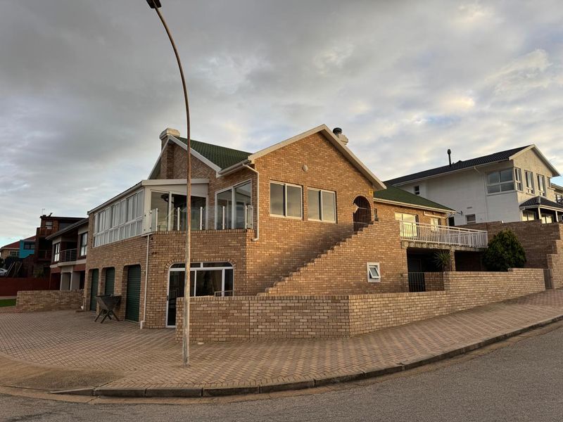 A multi-level brick house featuring a tiled roof, integrated garage, and an elevated balcony with glass balustrades, situated on a corner plot.