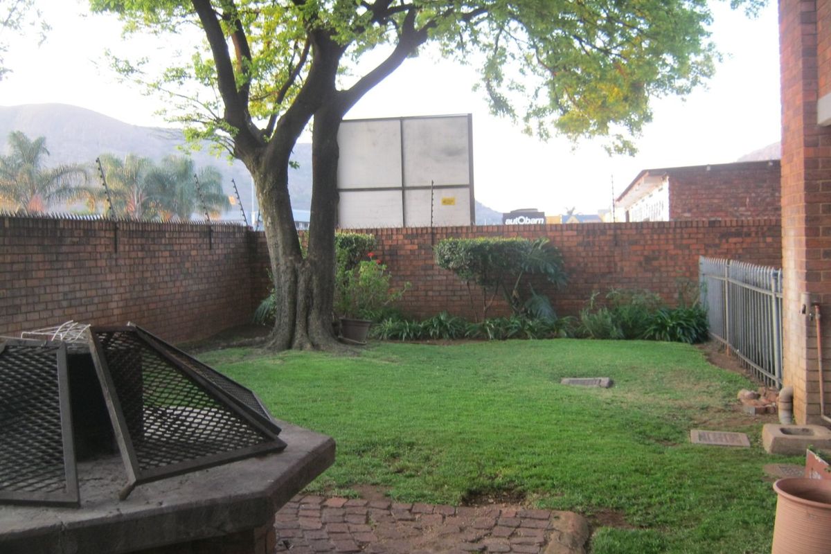 A private rear garden featuring a lawn, paved patio area with a built-in braai, and secure brick boundary walls with electric fencing.