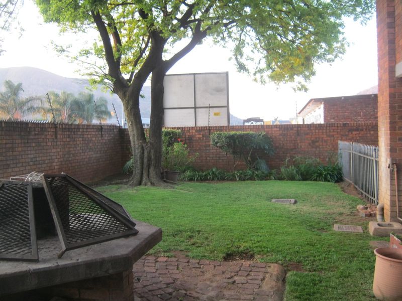 A private rear garden featuring a lawn, paved patio area with a built-in braai, and secure brick boundary walls with electric fencing.