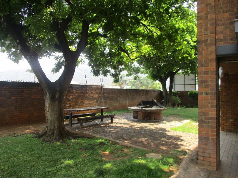 A private rear garden area featuring a paved patio, built-in braai, mature trees, and a secure brick boundary wall with electric fencing.