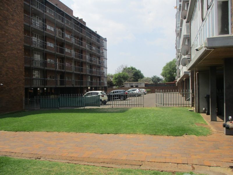 Exterior view of an apartment complex featuring brick facades, paved walkways, a central lawn area, and secure metal fencing.