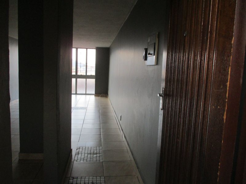 A vacant apartment hallway featuring tiled flooring, dark grey walls, and a wooden entrance door leading to an open living area.