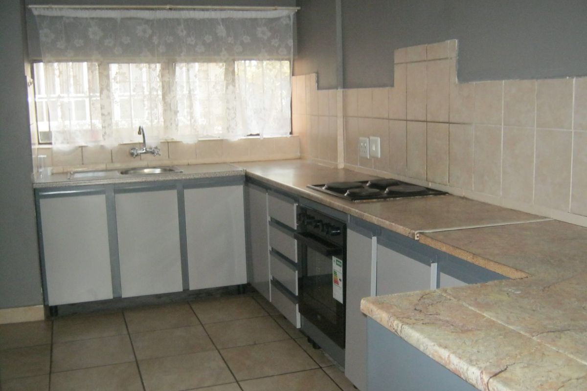 A functional kitchen featuring built-in cabinetry, laminate countertops, a tiled backsplash, and integrated oven and hob, with ceramic floor tiles throughout.