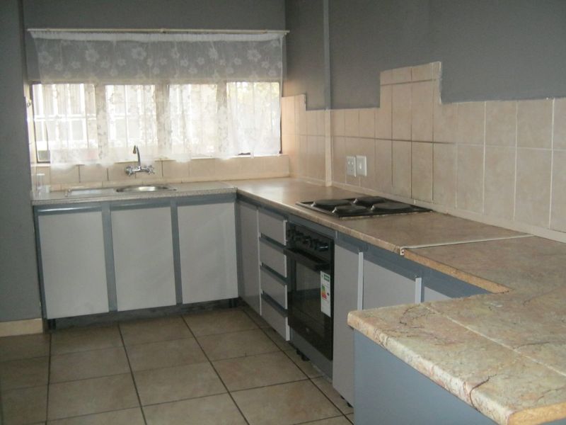A functional kitchen featuring built-in cabinetry, laminate countertops, a tiled backsplash, and integrated oven and hob, with ceramic floor tiles throughout.