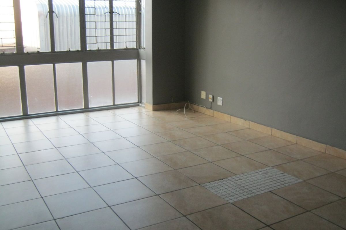 An empty living room featuring tiled flooring, large windows with security bars, and neutral grey walls.