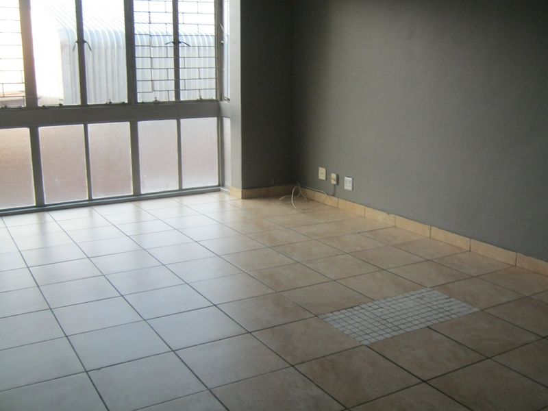 An empty living room featuring tiled flooring, large windows with security bars, and neutral grey walls.