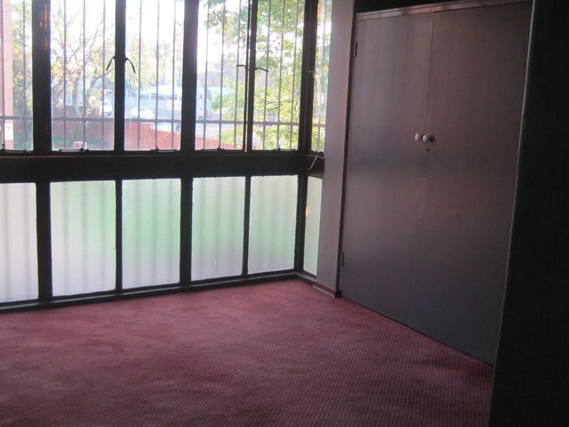 An empty bedroom featuring a built-in wardrobe, carpet flooring, and large windows with security bars.