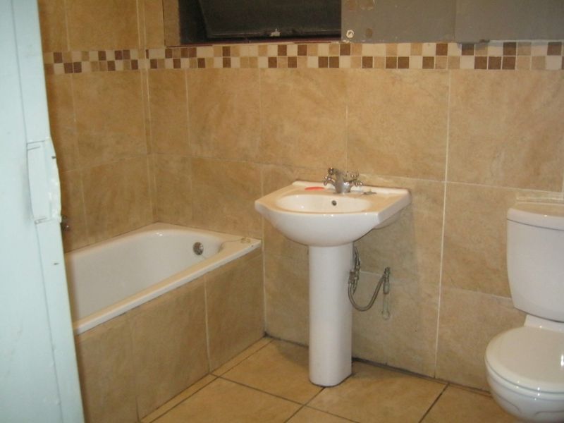 A dated bathroom featuring a pedestal basin, bathtub, and toilet with beige ceramic wall and floor tiling.