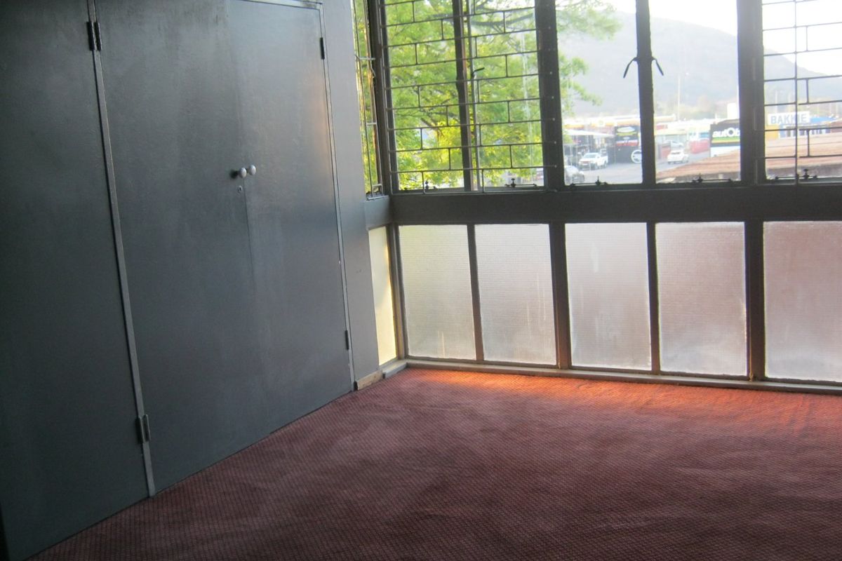 An empty bedroom featuring built-in cupboards, carpeted flooring, and large windows with metal security bars.