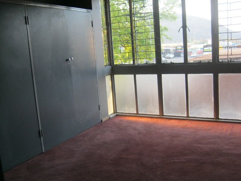 An empty bedroom featuring built-in cupboards, carpeted flooring, and large windows with metal security bars.