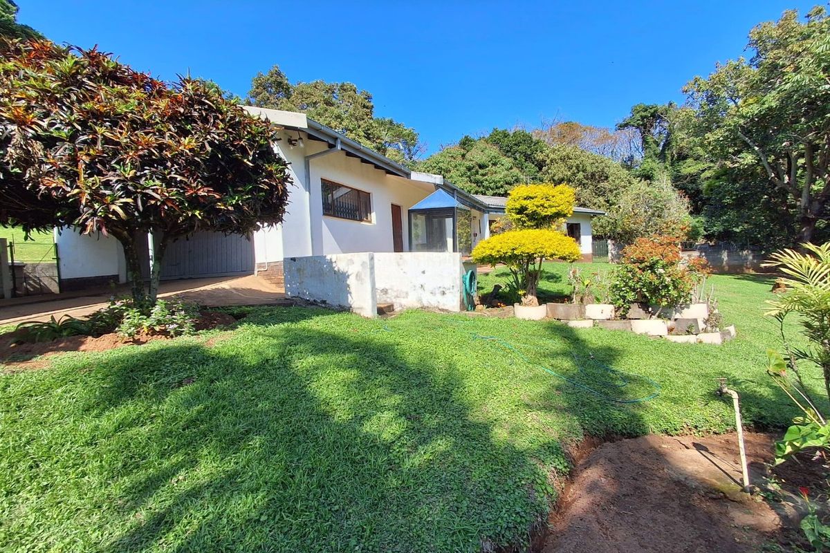Rear view of the property featuring a landscaped garden, concrete retaining wall, and access to the garage area.