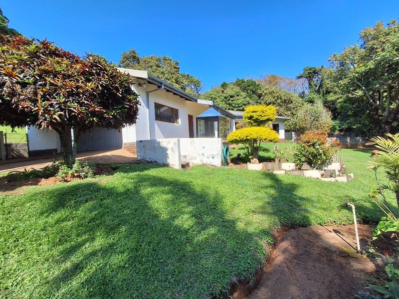 Rear view of the property featuring a landscaped garden, concrete retaining wall, and access to the garage area.