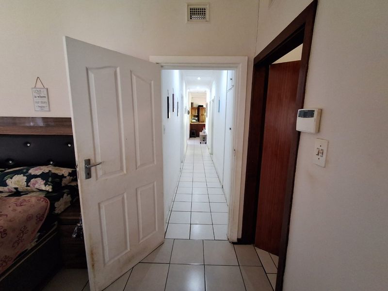 A tiled hallway connecting interior spaces, featuring standard door frames, an alarm system keypad, and a ceiling ventilation grille.