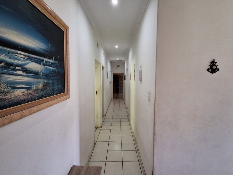 A long, tiled hallway featuring recessed downlighting and neutral wall finishes, providing access to multiple rooms within the home.
