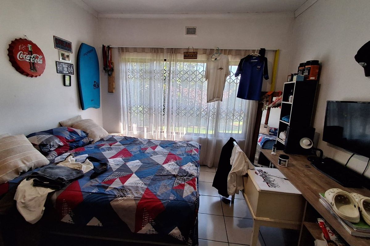 A functional bedroom featuring tiled flooring and a large window fitted with a security gate, providing natural light and ventilation.
