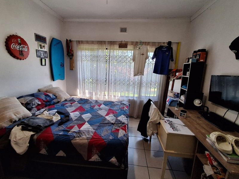 A functional bedroom featuring tiled flooring and a large window fitted with a security gate, providing natural light and ventilation.