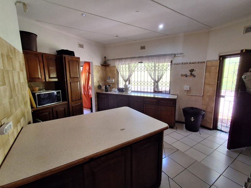 A functional kitchen featuring traditional wooden cabinetry, laminate countertops, tiled backsplash, and ceramic flooring with direct access to the exterior.