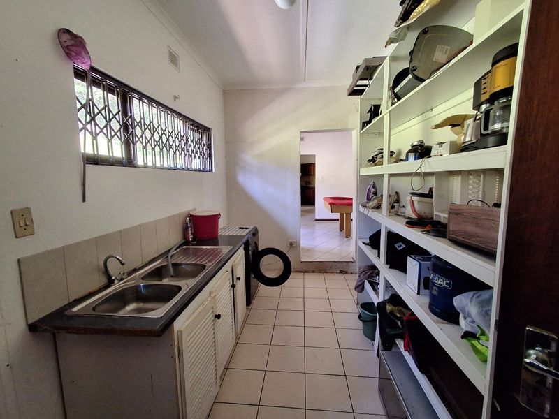 Functional scullery area featuring a double stainless steel sink, tiled splashback, and extensive built-in shelving for storage.