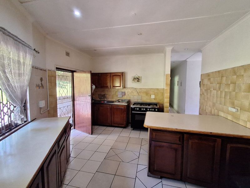 A functional kitchen featuring wooden cabinetry, tiled backsplash, and a freestanding oven, with direct access to the exterior via a security gate.
