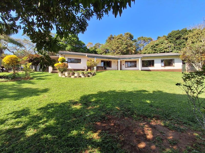 A view of the rear elevation of the house featuring a spacious lawn, established garden, and a covered patio area.