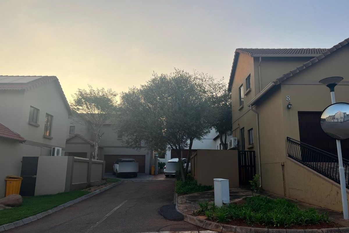 A view of the residential street approach featuring paved driveways, boundary walls, and established landscaping within a secure complex setting.