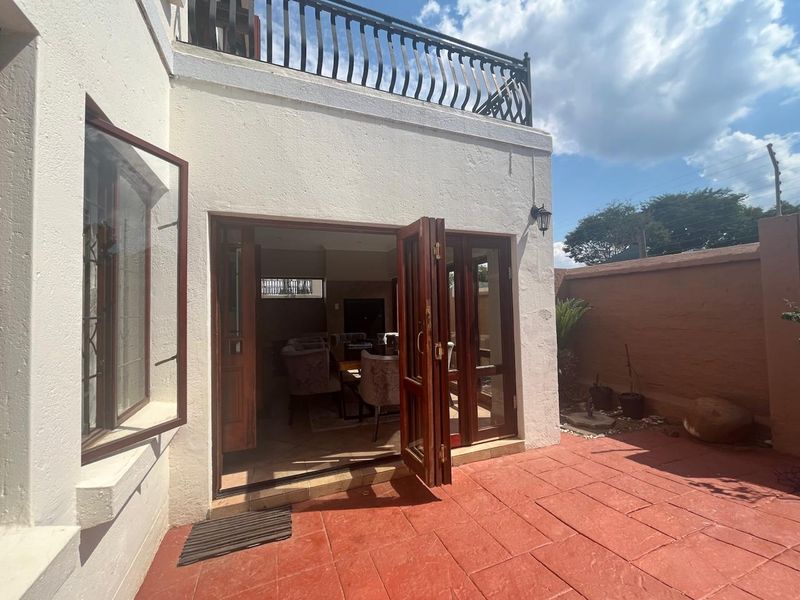 A rear exterior view featuring a tiled patio area, timber folding doors leading into the home, and a balcony with a wrought iron railing.