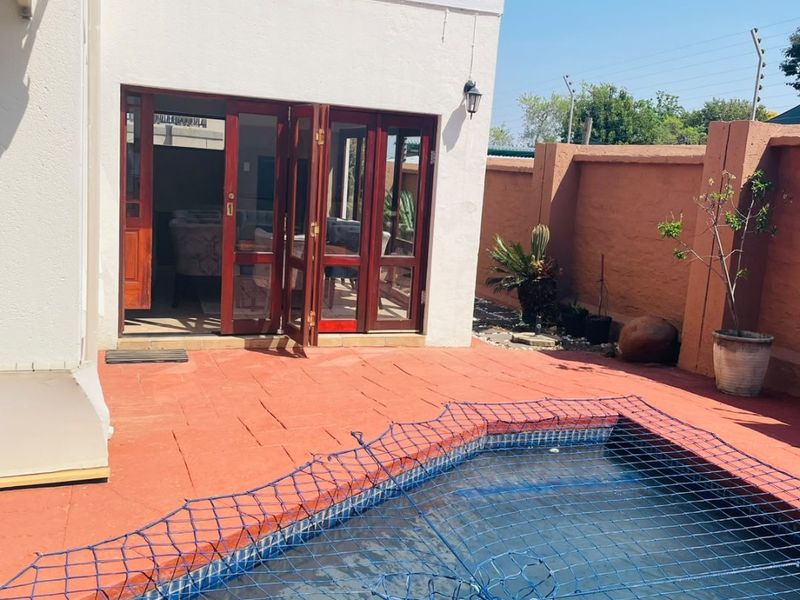 Outdoor pool area featuring a safety net, terracotta paving, and access to the main house via wooden folding doors with an upper balcony.