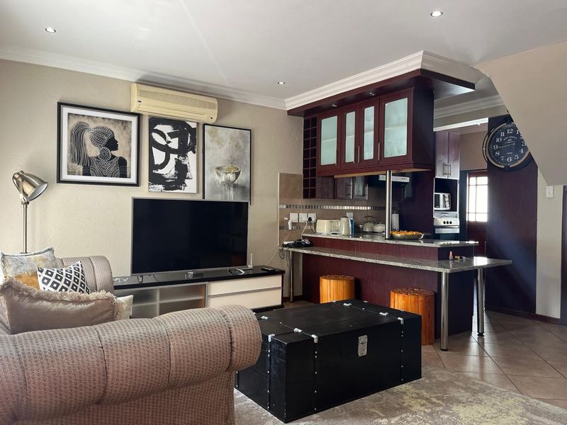 Open-plan living area featuring a kitchen with dark wood cabinetry, granite breakfast bar, tiled floors, and recessed lighting, seamlessly connected to the lounge space.