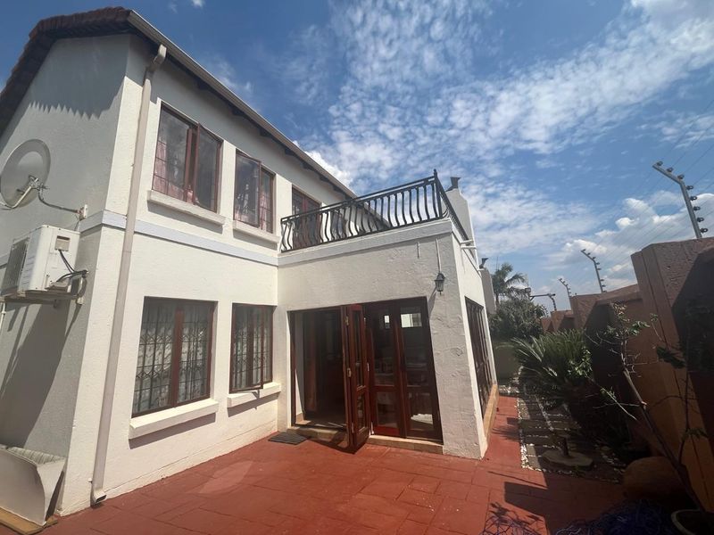 Rear view of the property featuring a tiled patio, timber-framed doors, and an upper-level balcony with wrought iron railings.