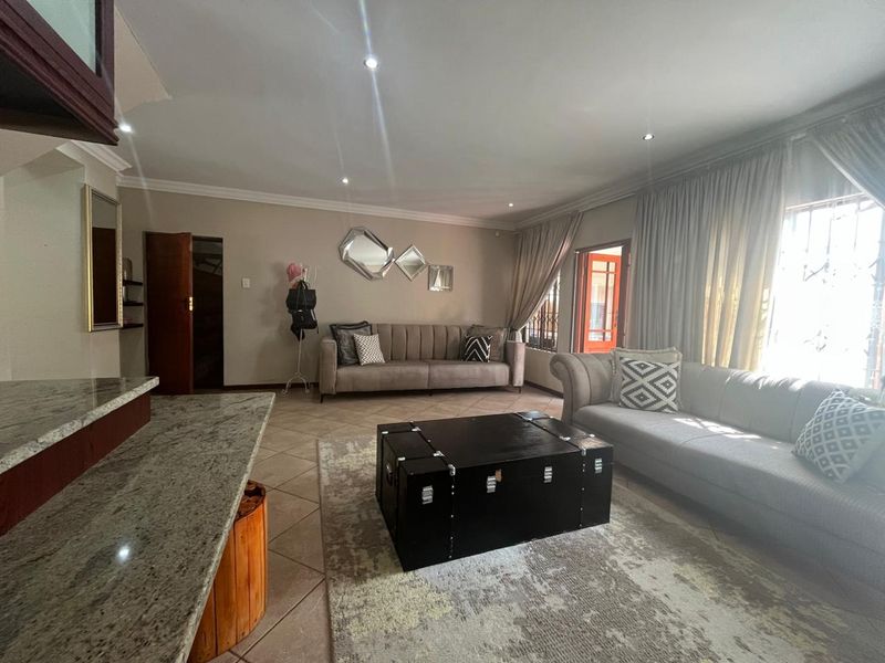 A spacious living room featuring tiled flooring, recessed downlighting, and a granite breakfast bar counter, with direct access to an outdoor area.
