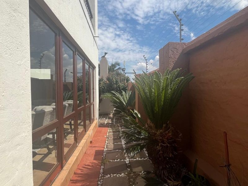 A narrow side garden path featuring paved stepping stones, a boundary wall with electric fencing, and large windows looking into the home.