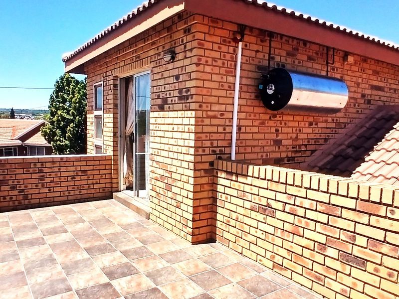 An elevated balcony featuring brick construction, tiled flooring, and a sliding door entrance, with an external geyser mounted on the exterior wall.