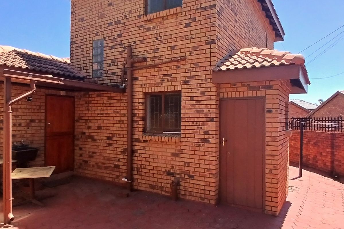 Rear view of a face brick house featuring a paved courtyard area, security bars on windows, and a brick boundary wall.