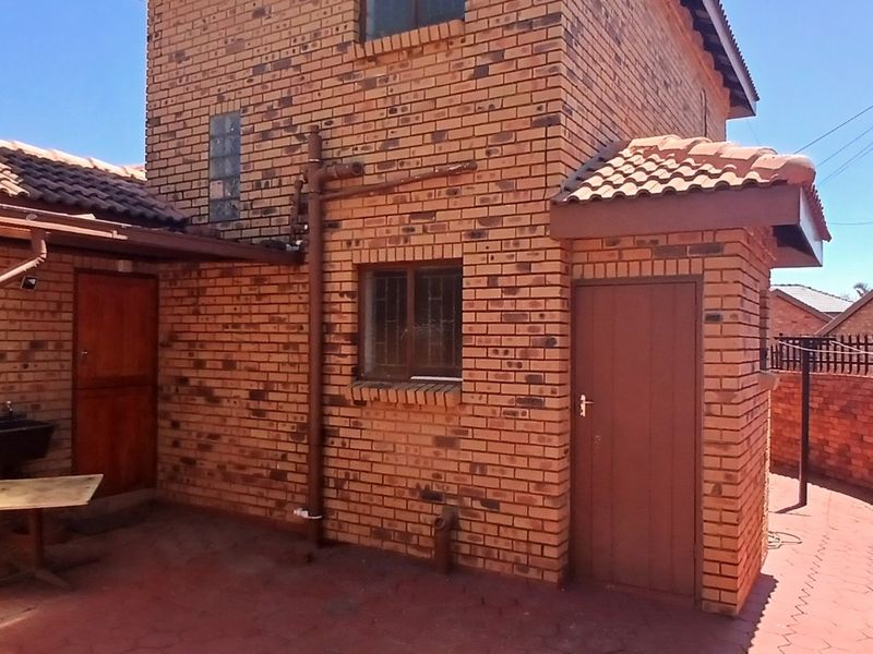 Rear view of a face brick house featuring a paved courtyard area, security bars on windows, and a brick boundary wall.