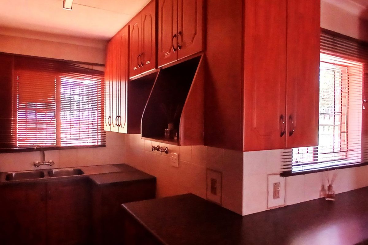 A functional kitchen featuring wooden cabinetry, laminate countertops, a double basin sink, and tiled backsplash, offering a classic layout with natural light.